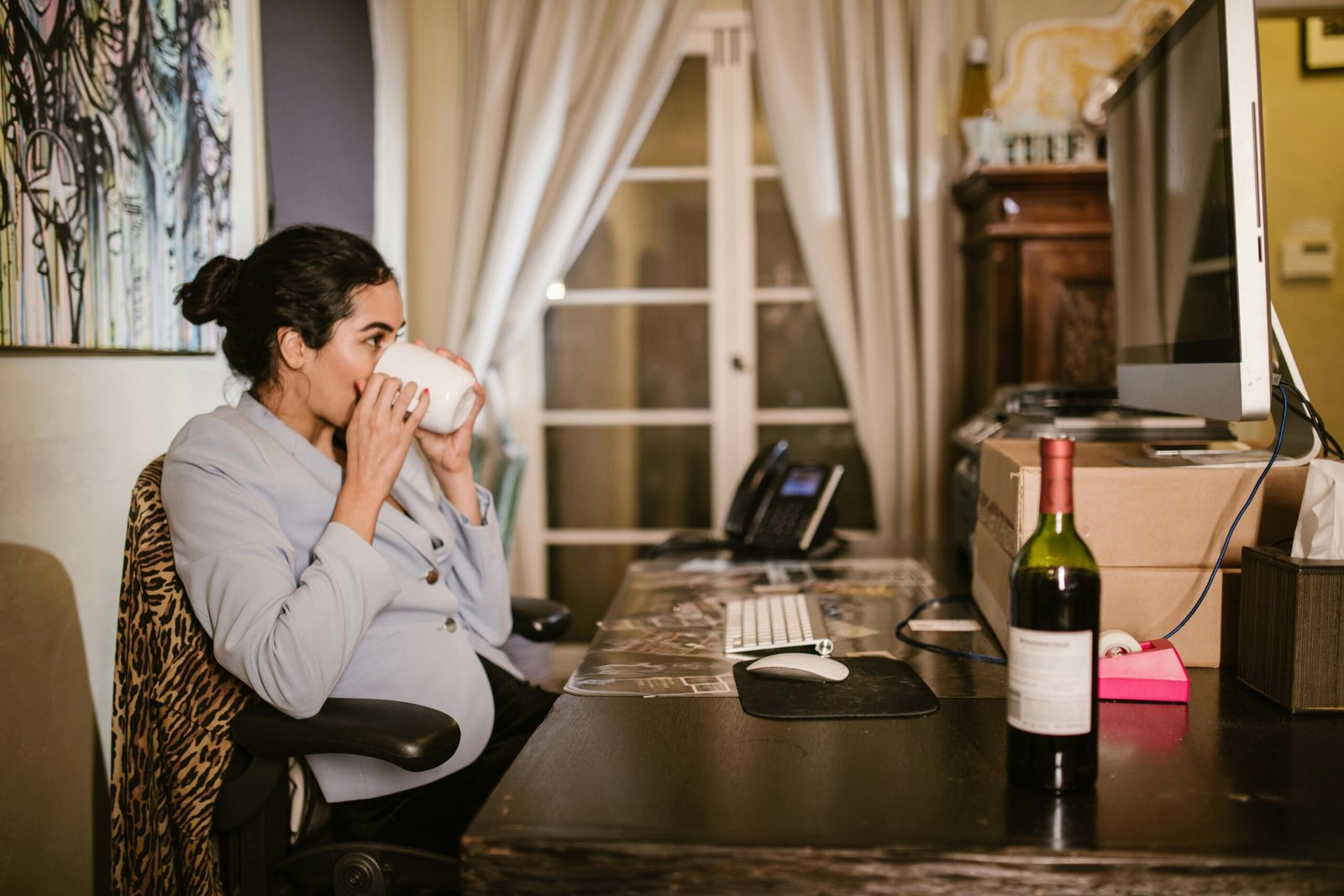 A Woman Drinking from a Mug Near Her Computer