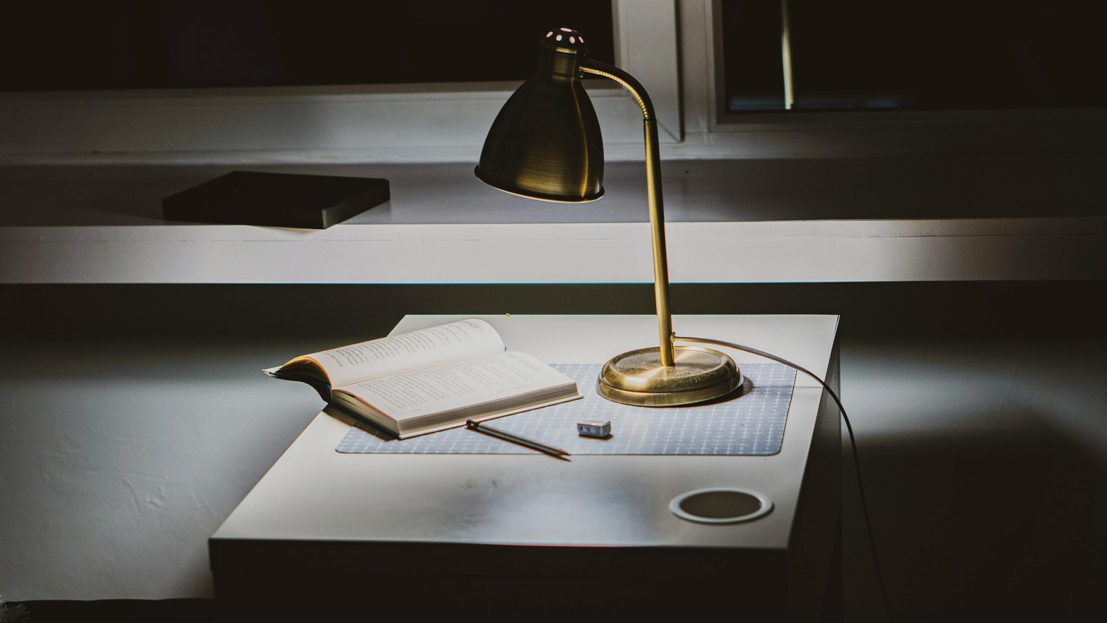 Powered-on Gold Desk Lamp on Desk With Opened Book